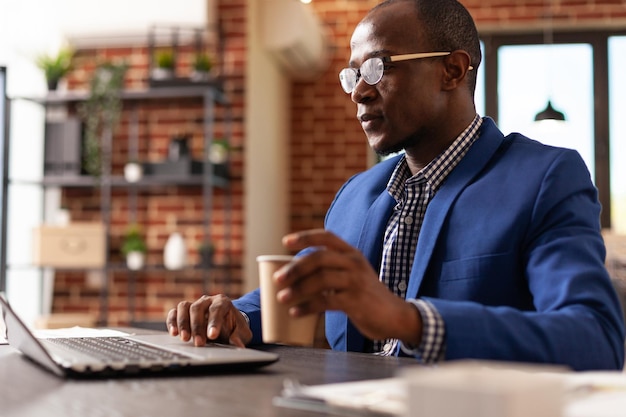 Afro-Amerikaanse man met laptop aan balie om bedrijfsstrategie te plannen. Ondernemer die op de computer werkt om het leiderschapsproject te analyseren, met een kopje koffie. Werknemer bij bedrijf baan