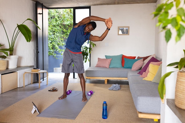 Afro-Amerikaanse man traint in de woonkamer, met behulp van tablet. Quality time alleen thuis doorbrengen.