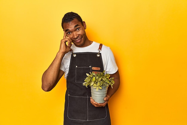 Afro-Amerikaanse man tuinier met plant gele studio wijzend tempel met vinger denken