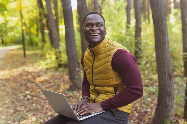 Afro-Amerikaanse man zit in het stadspark op een bankje met laptop die online buiten studeert man freela