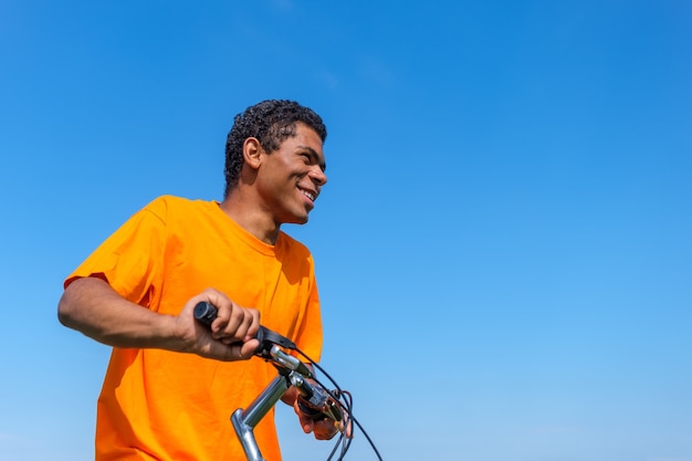 Afro-Amerikaanse man zit op de fiets buiten tegen de blauwe hemelachtergrond