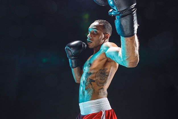 Afro-amerikaanse mannelijke bokser. jonge man bokstraining in een fitnessclub. gespierde sterke man op zwarte achtergrond studio