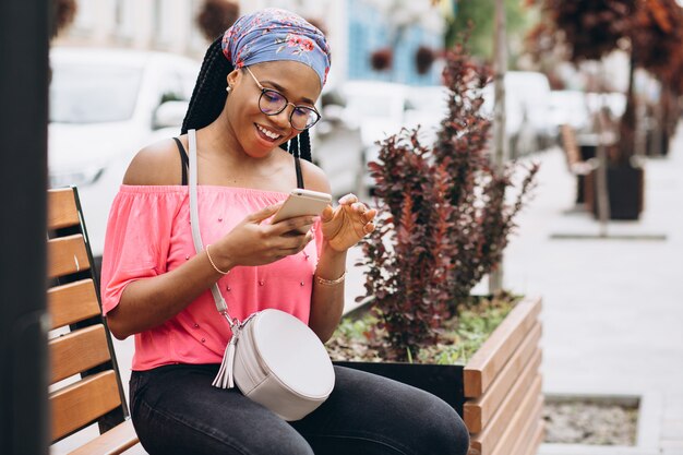 Afro-Amerikaanse meisje met behulp van haar mobiele telefoon zittend op houten bankje