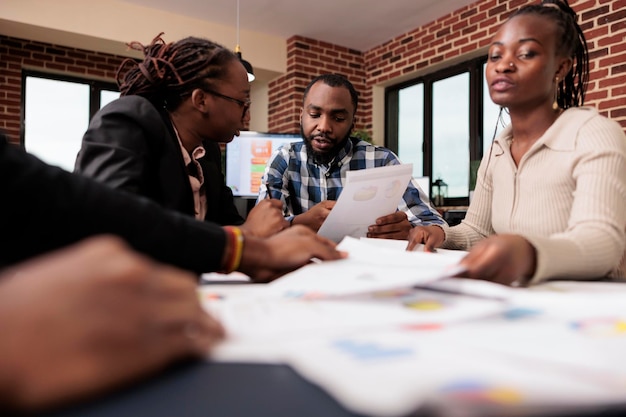 Afro-Amerikaanse mensen doen teamwerk op kantoor, werken met opstartdocumenten om bedrijfspresentaties te plannen en te rapporteren met onderzoeksgegevens. Analyseren van papieren documenten in de bestuurskamer.