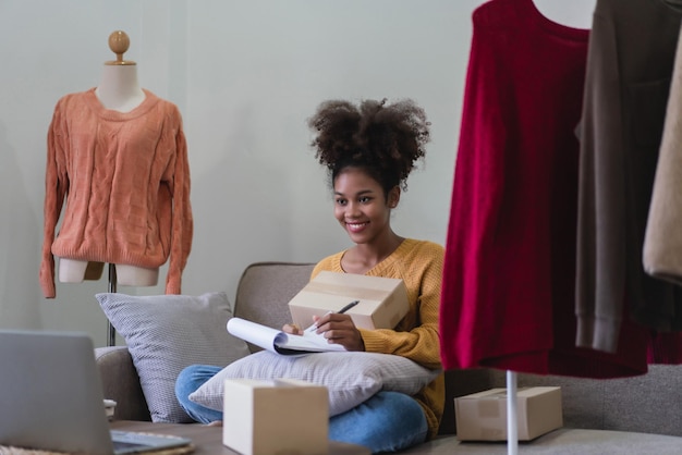 Foto afro-amerikaanse mode-handelaarsvrouw die een online bestelling schrijft en een pakketdoos klaarmaakt voor bezorging