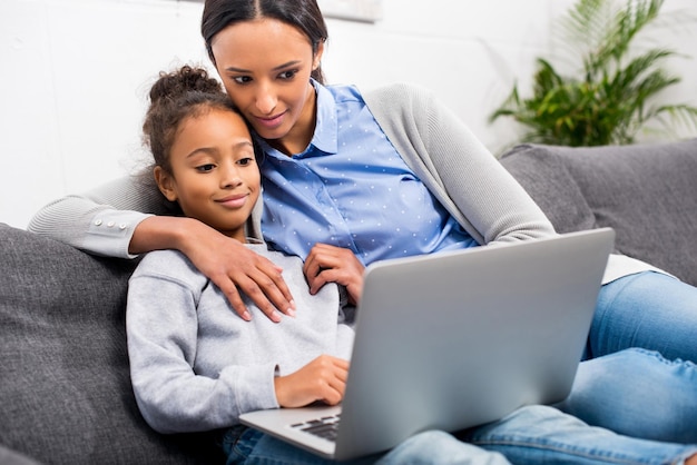 Afro-Amerikaanse moeder en dochter met een laptop thuis.