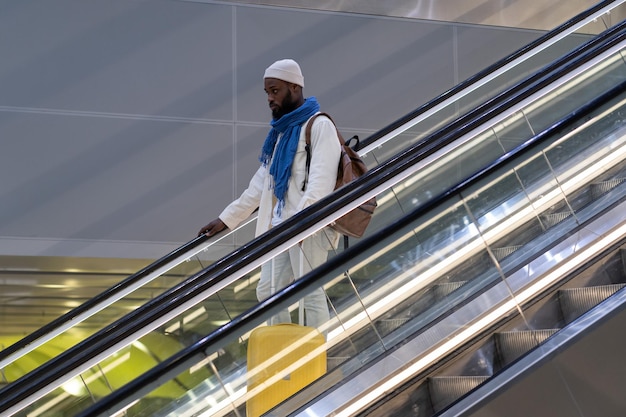 Afro-Amerikaanse passagier man met koffer staat op roltrap houdt leuning in luchthaventerminal