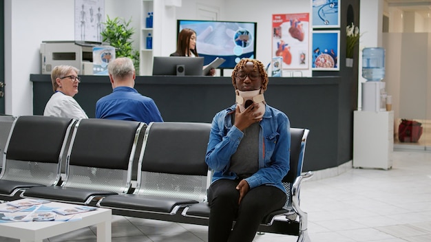 Afro-Amerikaanse patiënt met cervicaal nekschuim in het gezondheidscentrum, wachtend om een controlebezoek bij te wonen met de dokter. Jonge vrouw die medische halsband draagt na ongevalsverwonding in wachtkamer.