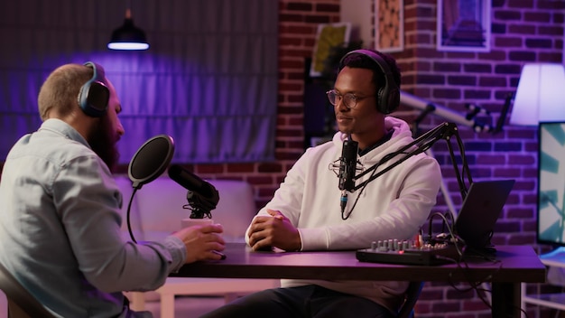 Afro-amerikaanse podcaster in interview met beroemde influencer-groetgast die vuiststoot doet in thuisstudio. internetradio-host die sociale media-vlogger ontmoet in live podcast in avondshow.