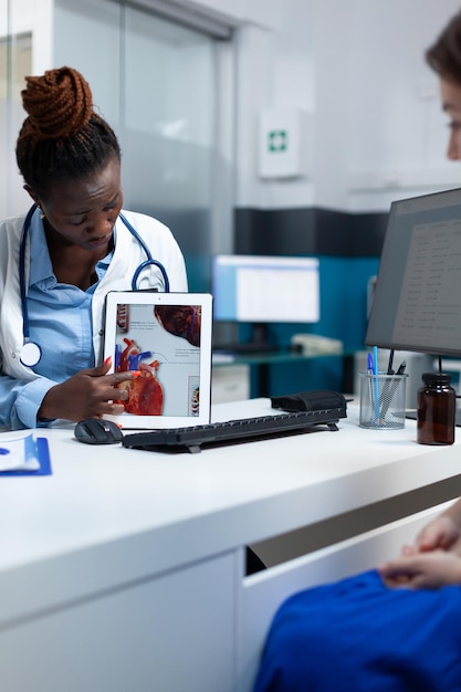 Afro-Amerikaanse radioloog arts met tablet die hartradiografie uitlegt en medische expertise bespreekt met geduldige vrouw tijdens klinische afspraak. Cardioloog werkzaam in ziekenhuis kantoor.