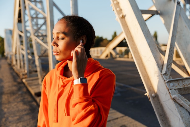 Afro-Amerikaanse rustige vrouw in sportkleding die oordoppen gebruikt tijdens het trainen op de oude brug