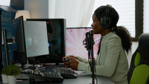 Afro-Amerikaanse space shooter-speler blij na het winnen van virtuele competitie met krachtige RGB-computer. Online streaming cyber optreden tijdens videogametoernooi in huis met neonlichten.