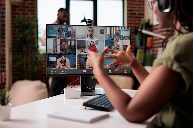 Afro-Amerikaanse startup-medewerker die vanuit huis werkt, gebarend in videoconferentie met collega's aan de balie. Eigenaar van een klein bedrijf praat met team in internetoproep op personal computer met webcam.