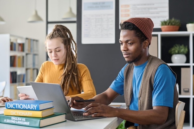 Afro-amerikaanse student doet taak online op laptop terwijl hij in de klas studeert met zijn klasgenoten