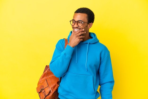 Afro-Amerikaanse student man over geïsoleerde gele achtergrond op zoek naar de zijkant