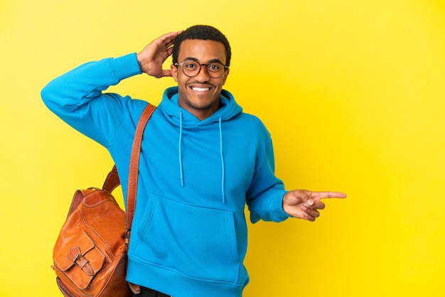 Afro-Amerikaanse student man over geïsoleerde gele achtergrond verrast en wijzende vinger naar de zijkant