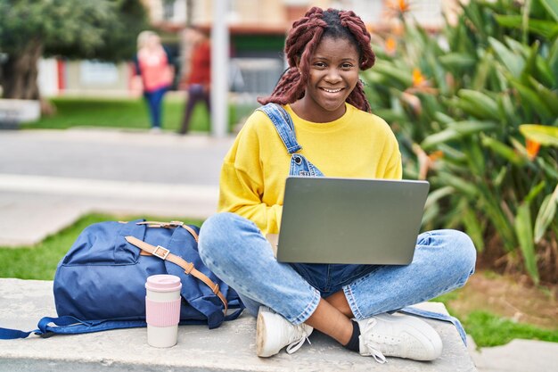 Afro-Amerikaanse studente met behulp van laptop zittend op een bankje op campus park
