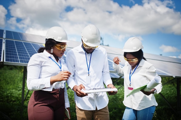 Afro-amerikaanse technicus controleert het onderhoud van de zonnepanelen. groep van drie zwarte ingenieurs die bij zonnestation bijeenkomen.