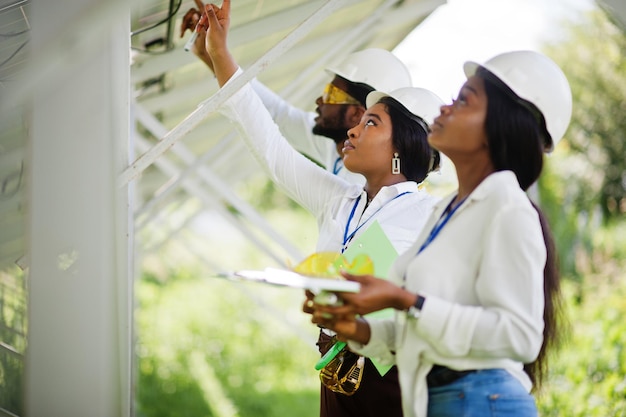 Afro-Amerikaanse technicus controleert het onderhoud van de zonnepanelen. Groep van drie zwarte ingenieurs die bij zonnestation bijeenkomen.