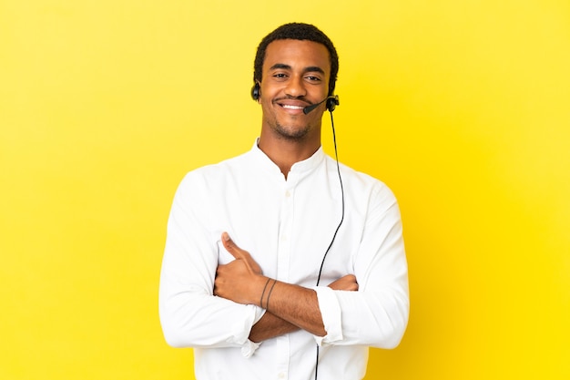 Afro-amerikaanse telemarketeer man aan het werk met een headset over geïsoleerde gele achtergrond die de armen gekruist houdt in frontale positie