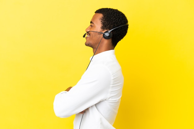 Afro-Amerikaanse telemarketeer man aan het werk met een headset over geïsoleerde gele achtergrond in laterale positie