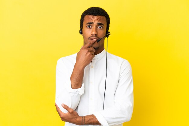 Afro-Amerikaanse telemarketeer man aan het werk met een headset over geïsoleerde gele muur verrast en geschokt terwijl hij naar rechts kijkt looking