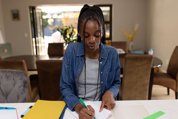 Afro-amerikaanse tiener meisje aan tafel zitten en huiswerk maken