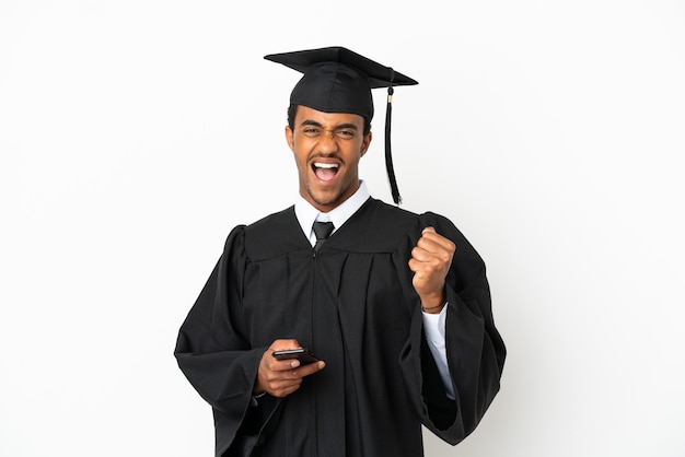 Afro-amerikaanse universitair afgestudeerde man over geïsoleerde witte achtergrond met telefoon in overwinningspositie