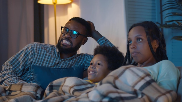 Afro-Amerikaanse vader, moeder en zoontje kijken 's avonds thuis tv