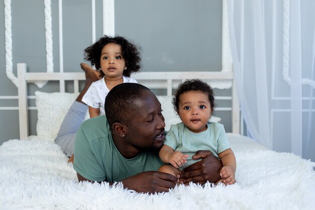 Afro-amerikaanse vader speelt met kinderen, baby's thuis op het bed in de slaapkamer en knuffelt, vaders liefde