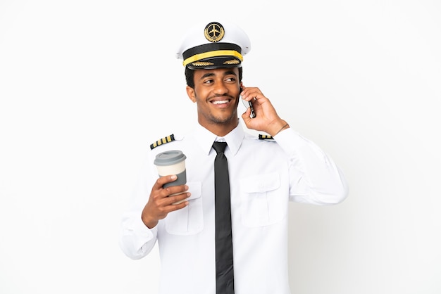 Afro-Amerikaanse vliegtuigpiloot over geïsoleerde witte achtergrond met koffie om mee te nemen en een mobiel