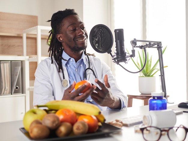 Afro-Amerikaanse voedingsdeskundige die naar de camera kijkt en gezond fruit laat zien in het consult