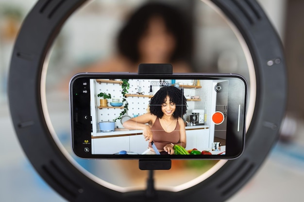 Afro-Amerikaanse vrouw chef-kok vlogger schiet koken voedsel vlog blog op smartphone thuis keuken Jonge vrouw record recept of tutorial op mobiele telefoon voorbereiding van gezonde vegetarische schotel