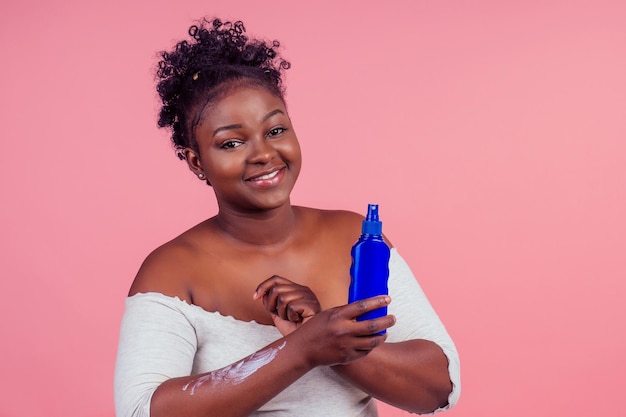Afro-Amerikaanse vrouw die crème aanbrengt tussen twee producten in studio roze achtergrond.