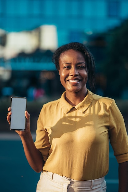 Afro-Amerikaanse vrouw die een smartphone toont terwijl ze in de straat van de stad staat