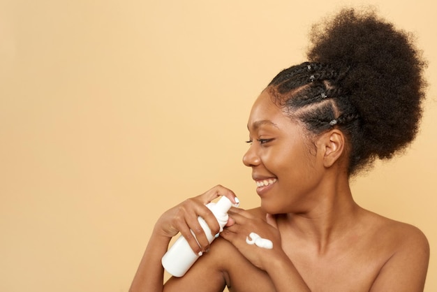 Afro-Amerikaanse vrouw die gezichtsreinigingsschuim op haar hand op een beige achtergrond toepast