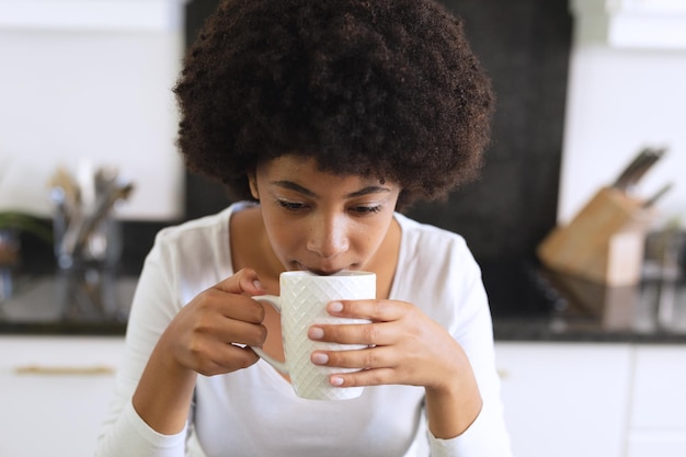 Afro-Amerikaanse vrouw die in de keuken koffie zit te drinken