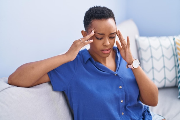 Afro-Amerikaanse vrouw die lijdt aan hoofdpijn terwijl ze thuis op de bank zit