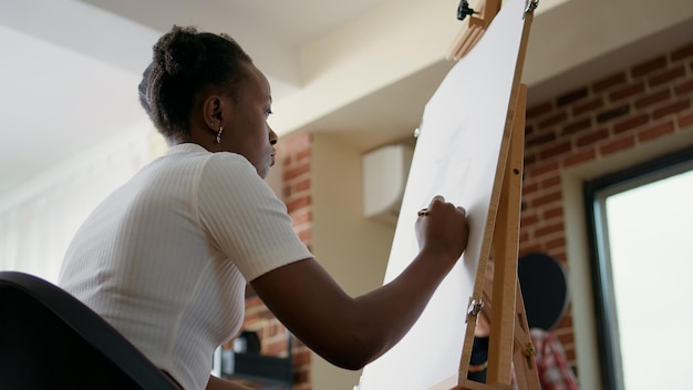 Afro-Amerikaanse vrouw die potlood gebruikt om vaasschets op canvas te tekenen, met aandacht voor kunstenaar die tekenles in de kunstles uitlegt. Student die workshop bijwonen als goede voornemens voor het nieuwe jaar.