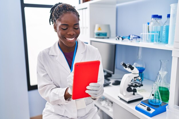 Afro-Amerikaanse vrouw die wetenschapperuniform draagt met behulp van touchpad in het laboratorium