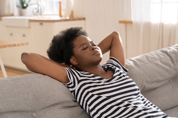 Afro-amerikaanse vrouw draag gestreept t-shirt slapen op de bank met arm onder het hoofd thuis. rust uit.