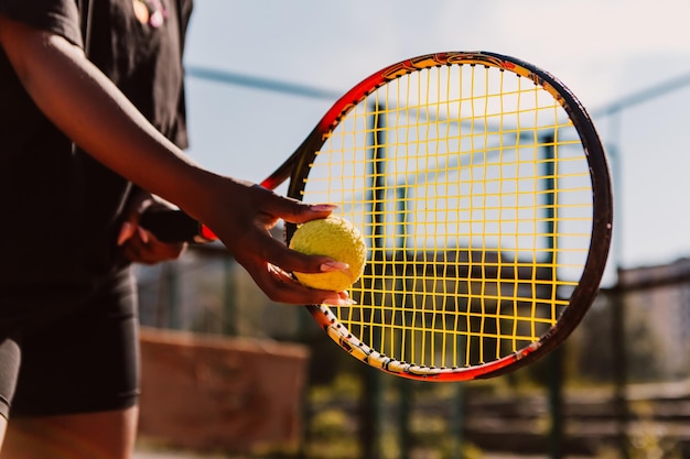 Afro-amerikaanse vrouw houdt racket en geelgroene bal tenniswedstrijd op gravelbaan