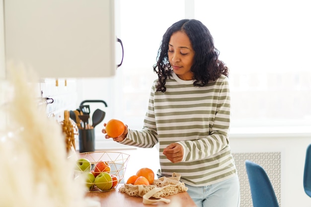 Afro-amerikaanse vrouw in de keuken die appels en sinaasappels sorteert na het winkelen in de supermarkt