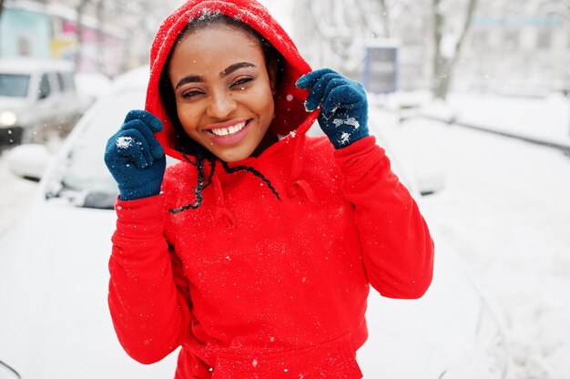 Afro-Amerikaanse vrouw in rode hoodie schone auto uit sneeuw in winterdag.