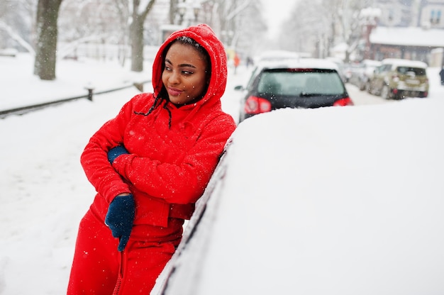 Afro-Amerikaanse vrouw in rode hoodie schone auto uit sneeuw in winterdag.