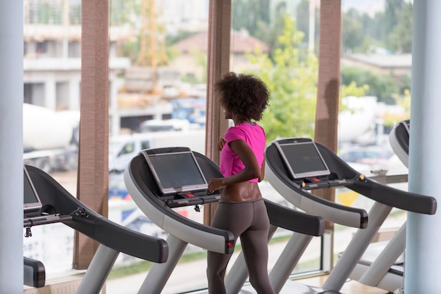 Afro-Amerikaanse vrouw loopt op een loopband in de sportschool terwijl ze naar muziek luistert via een koptelefoon