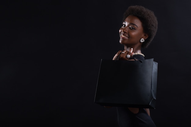 Afro-Amerikaanse vrouw met afro-kapsel houdt zwarte boodschappentassenverkoop en kortingen op markt en black friday-concept