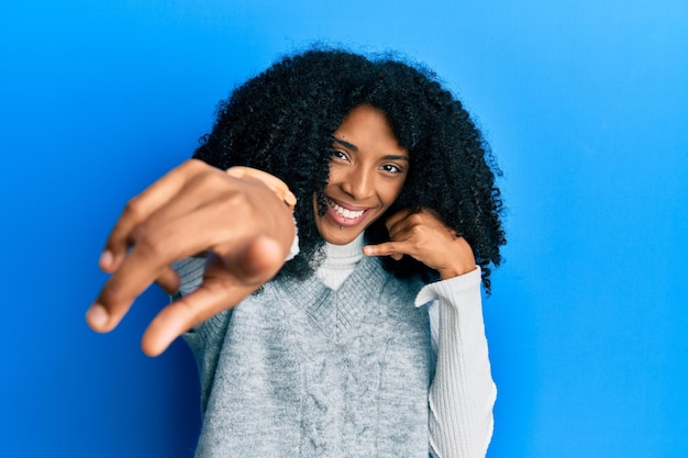 Afro-amerikaanse vrouw met afrohaar met een casual wintertrui die glimlacht terwijl ze een telefoongesprek voert