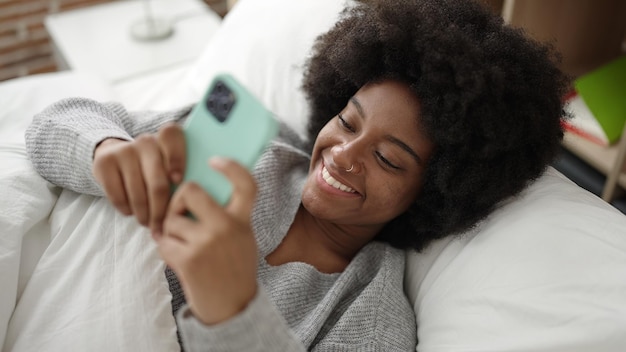 Afro-Amerikaanse vrouw met behulp van smartphone liggend op bed in de slaapkamer