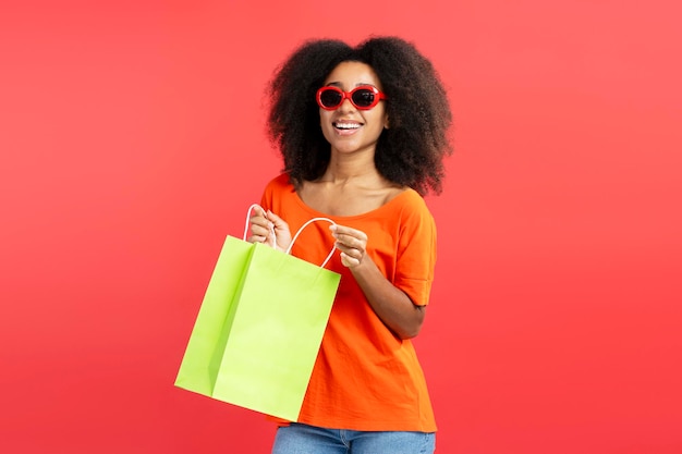 Afro-Amerikaanse vrouw met bril met boodschappentas geïsoleerd op rode achtergrond mockup